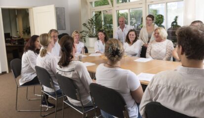 Teamrunde im Besprechungsraum, mehrere Mitarbeitende sitzen und lachen gemeinsam